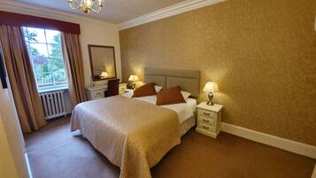 A hotel room with a large bed, two bedside tables with lamps, a dresser, a mirror, and a window with curtains.