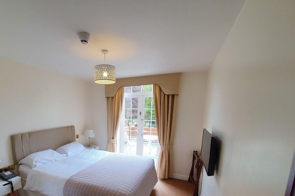 Habitación de hotel con cama, escritorio con lámpara, televisión en la pared y ventana con cortinas.