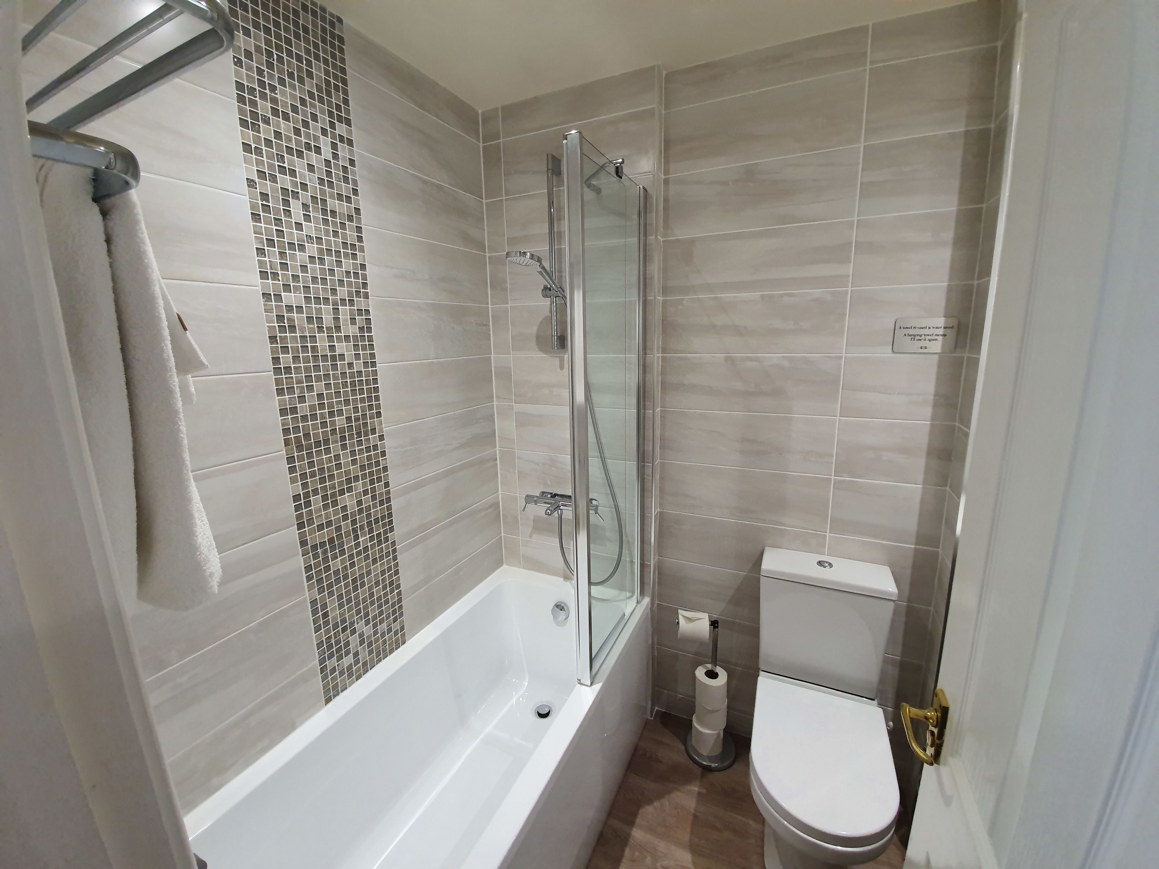 A modern bathroom with a bathtub, glass shower enclosure, toilet, and a toilet paper holder.