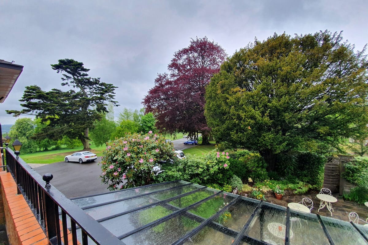 A conservatory with a glass roof, a brick balcony, and a view of a residential street with cars and trees.