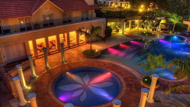 A resort with a swimming pool, palm trees, and a well-lit building. - Country Roads (Uluberiya)
