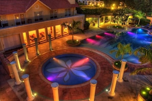 A resort with a swimming pool, palm trees, and a well-lit building. - Country Roads (Uluberiya)