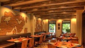 A restaurant with wooden ceiling beams, brick wall murals, and tables set with orange napkins. - Country Roads (Uluberiya)