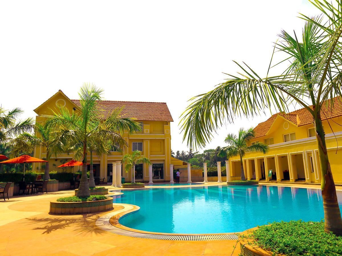 A swimming pool surrounded by palm trees and yellow buildings with a tiled roof.