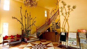 A lobby with a staircase, a sofa with red cushions, a geometric patterned floor, and bamboo decorations. - Country Roads (Uluberiya)