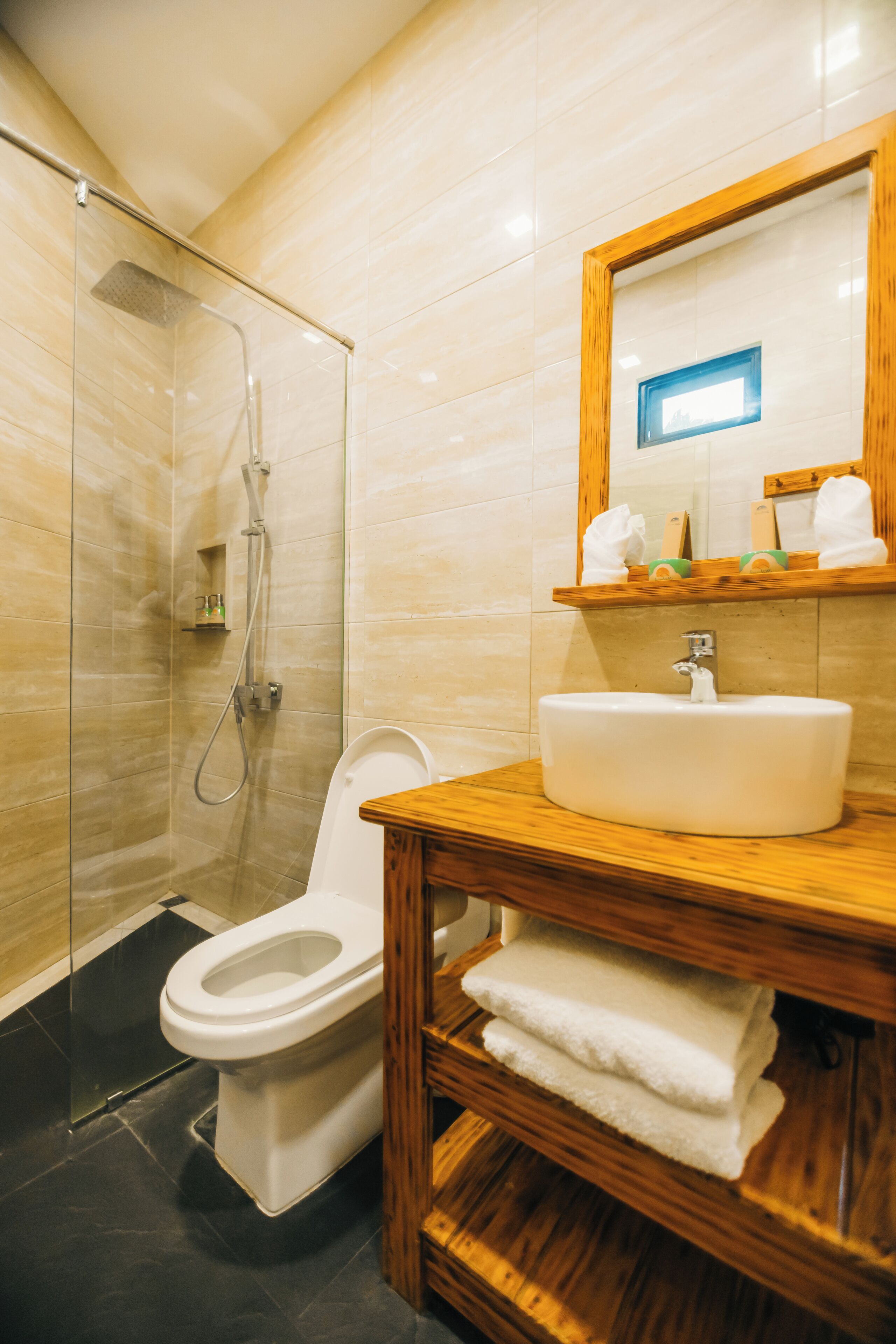 Un baño moderno con ducha acristalada, inodoro blanco, tocador de madera con lavamanos y un espejo sobre el tocador.
