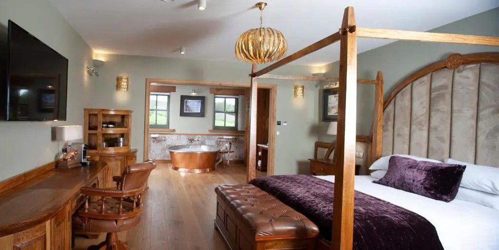 Une chambre à coucher avec un lit à baldaquin, un banc en bois, une baignoire et un coin repas comprenant une table et des chaises en bois.