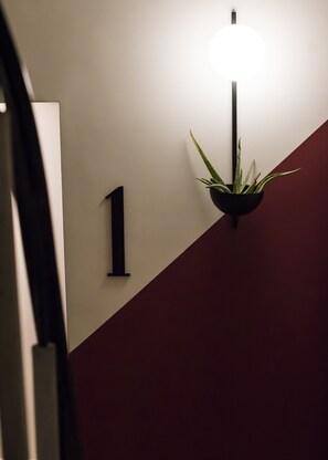 Um sinal de número '1' fixado na parede e um vaso com planta, com um aparelho de iluminação acima.