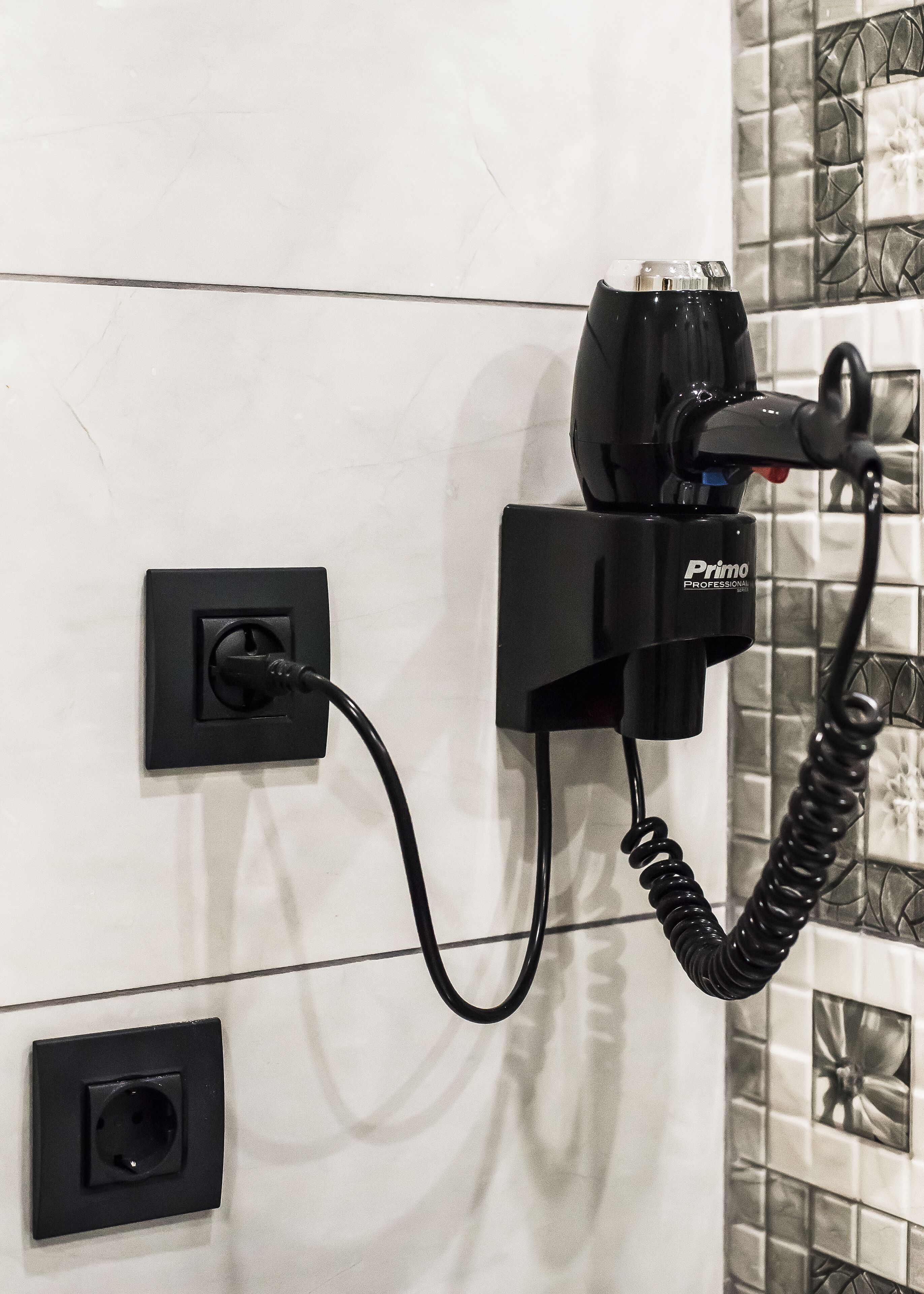 A black power strip with a cable plugged in, mounted on a wall with a tiled backsplash.