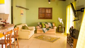 A living room with a sofa, chairs, a coffee table, a ceiling fan, a window with shutters, and a television on a stand. - Chalé Jaguanum (Mangaratiba)