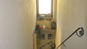 A narrow stairway with a handrail, a small window at the top, and a shelf with various decorative items. - B&B Cà Pavaglione (Castino)