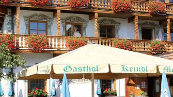 Ein traditionelles Gebäude mit hölzernen Balkonen, die mit Blumen geschmückt sind, Sitzgelegenheiten im Freien mit Tischen und Bänken, und einem Schild mit dem Namen einer lokalen Biersorte.