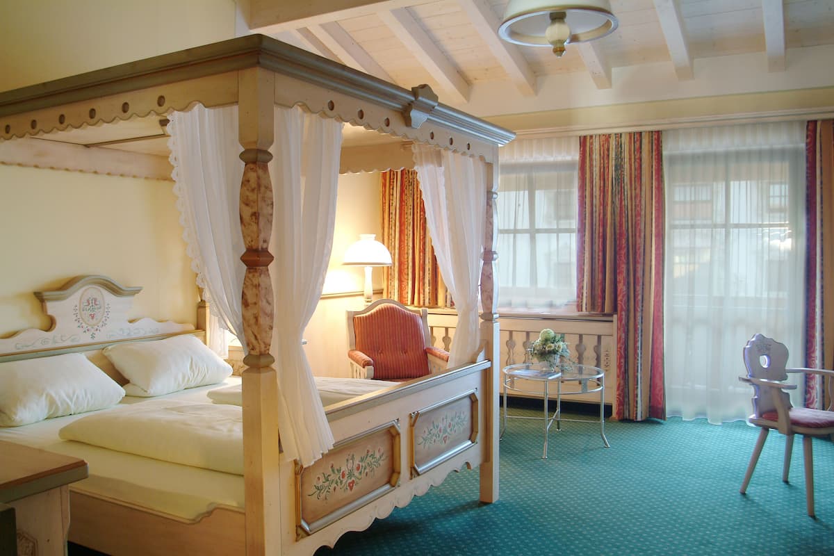 A four-poster bed with a canopy, a chair, a small table, and a window with curtains.