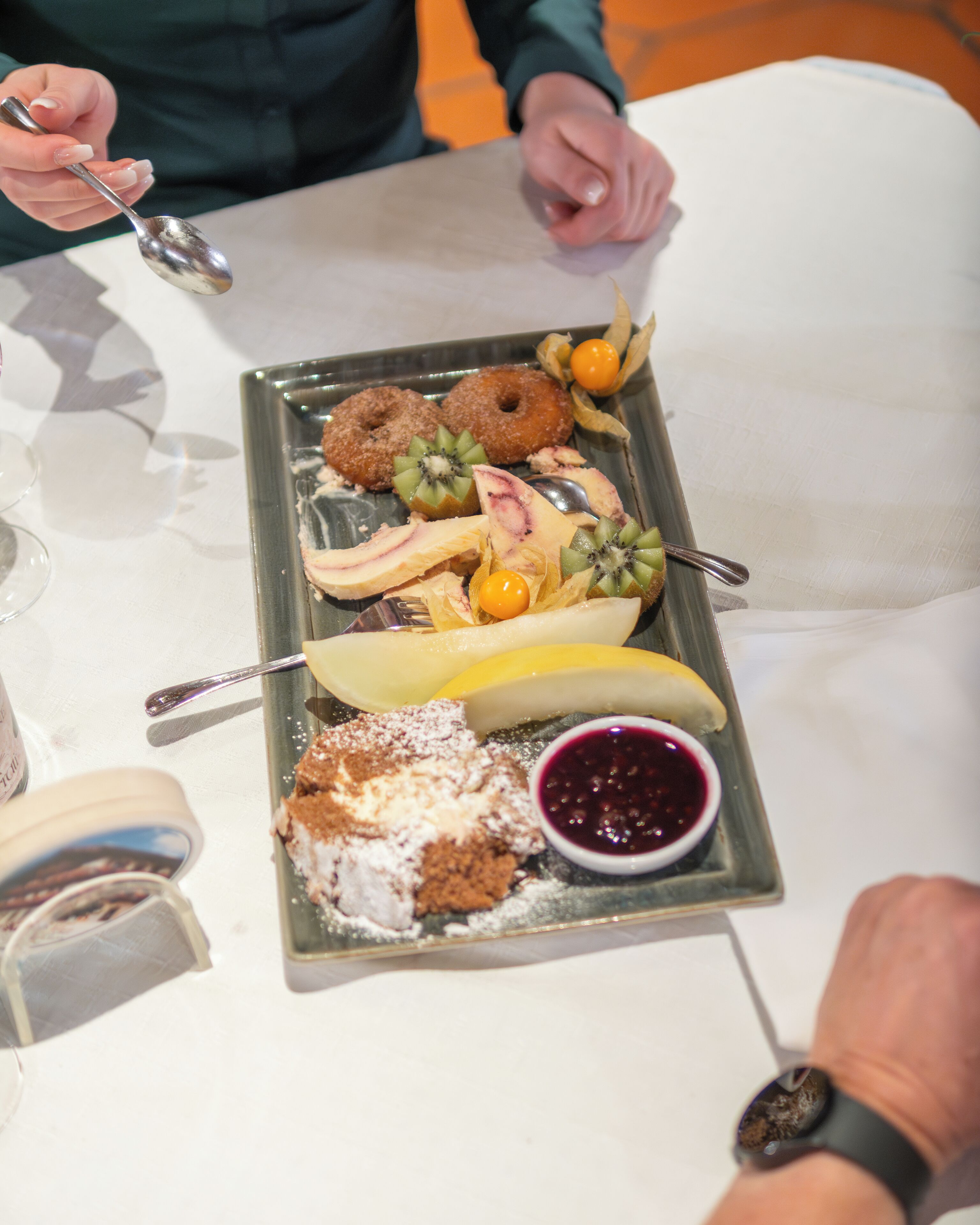 A dessert tray with various sweets and a small bowl of jam on a white table.
