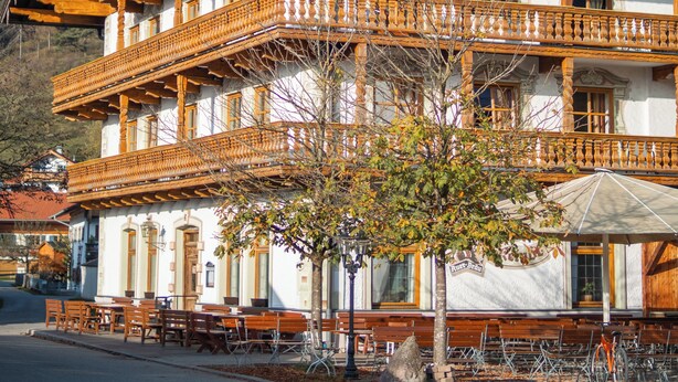 A traditional wooden building with a balcony, a mountain backdrop, and outdoor seating. - Hotel Gasthof Metzgerei Keindl (Oberaudorf)