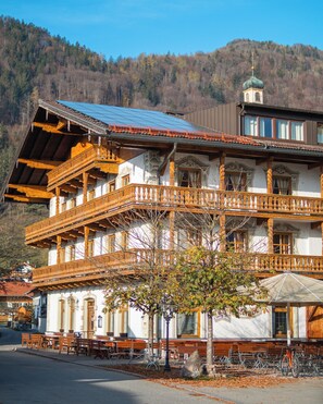 A traditional wooden building with a balcony, a mountain backdrop, and outdoor seating. - Hotel Gasthof Metzgerei Keindl (Oberaudorf)