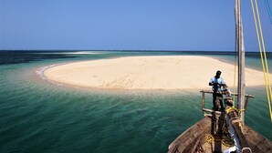 A sandy beach with clear turquoise water, a wooden boat with ropes, and a person standing on the boat. - Miti Miwiri (Ibo)