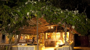 An outdoor bar area with a thatched roof, wooden seating, and a stone pathway leading to the entrance. - Miti Miwiri (Ibo)