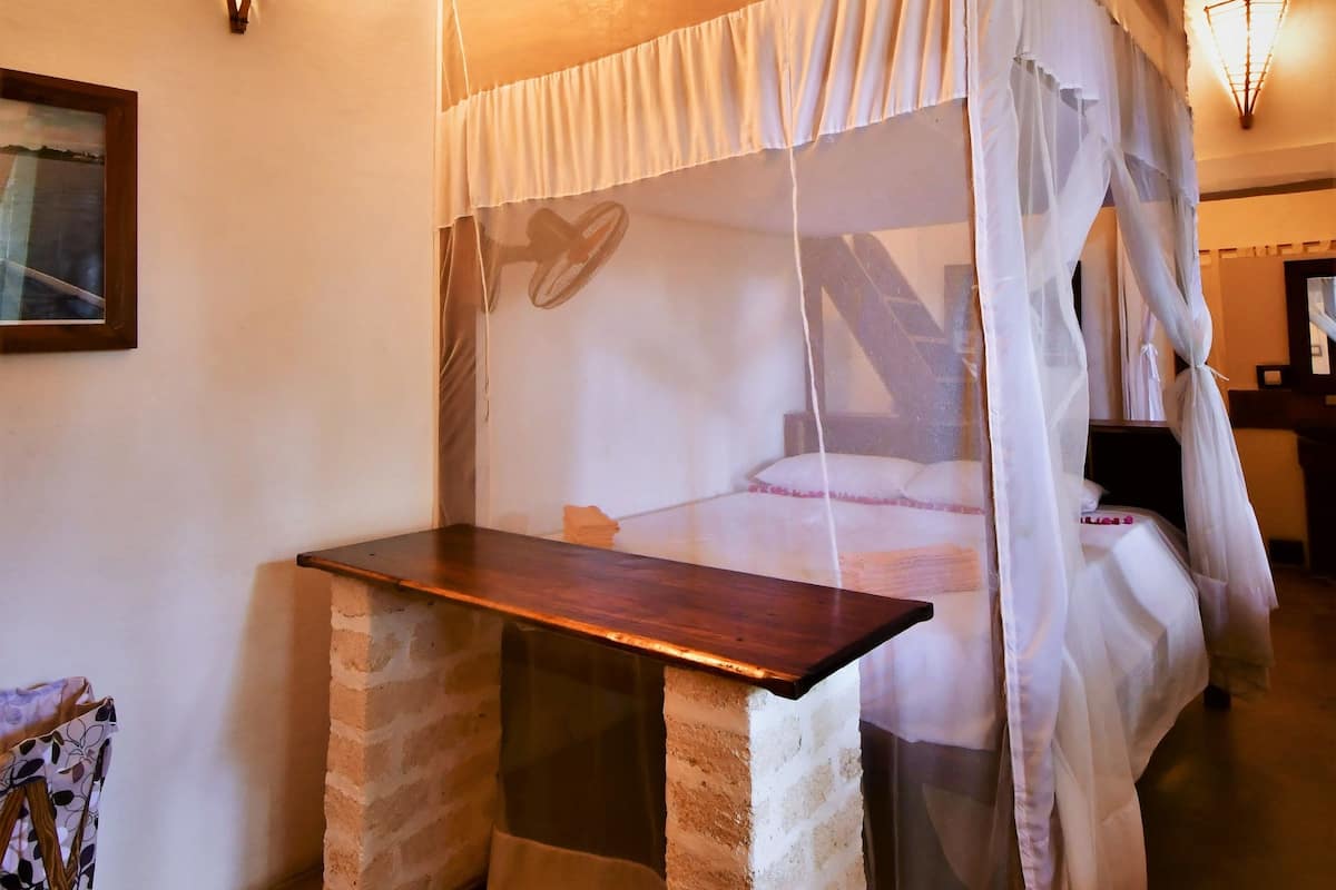Una habitación con una cama con dosel, un banco de madera y una lámpara fijada a la pared.