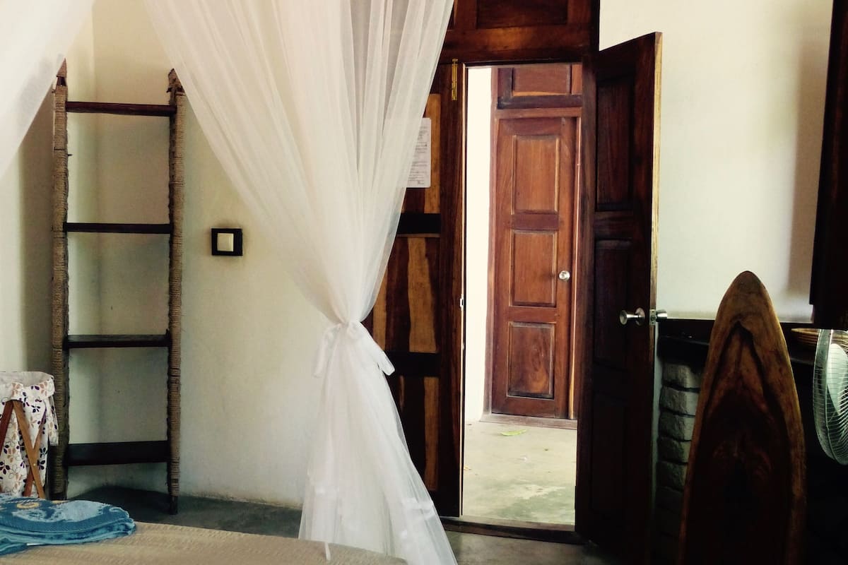 Un dormitorio con cama, una escalera de madera, una puerta de madera y un ventilador.