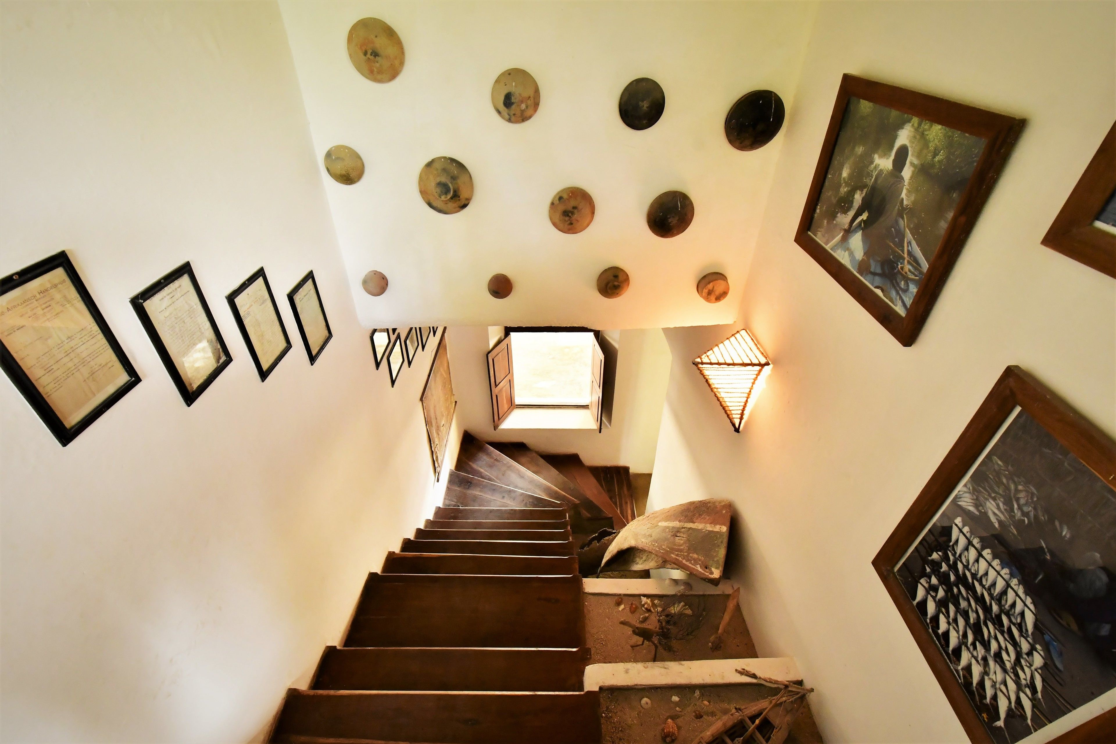 Una escalera con certificados enmarcados en la pared, un cuadro enmarcado y una lámpara decorativa.