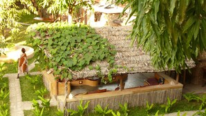 A traditional hut with a thatched roof, surrounded by a garden with various plants and a stone pathway. - Miti Miwiri (Ibo)