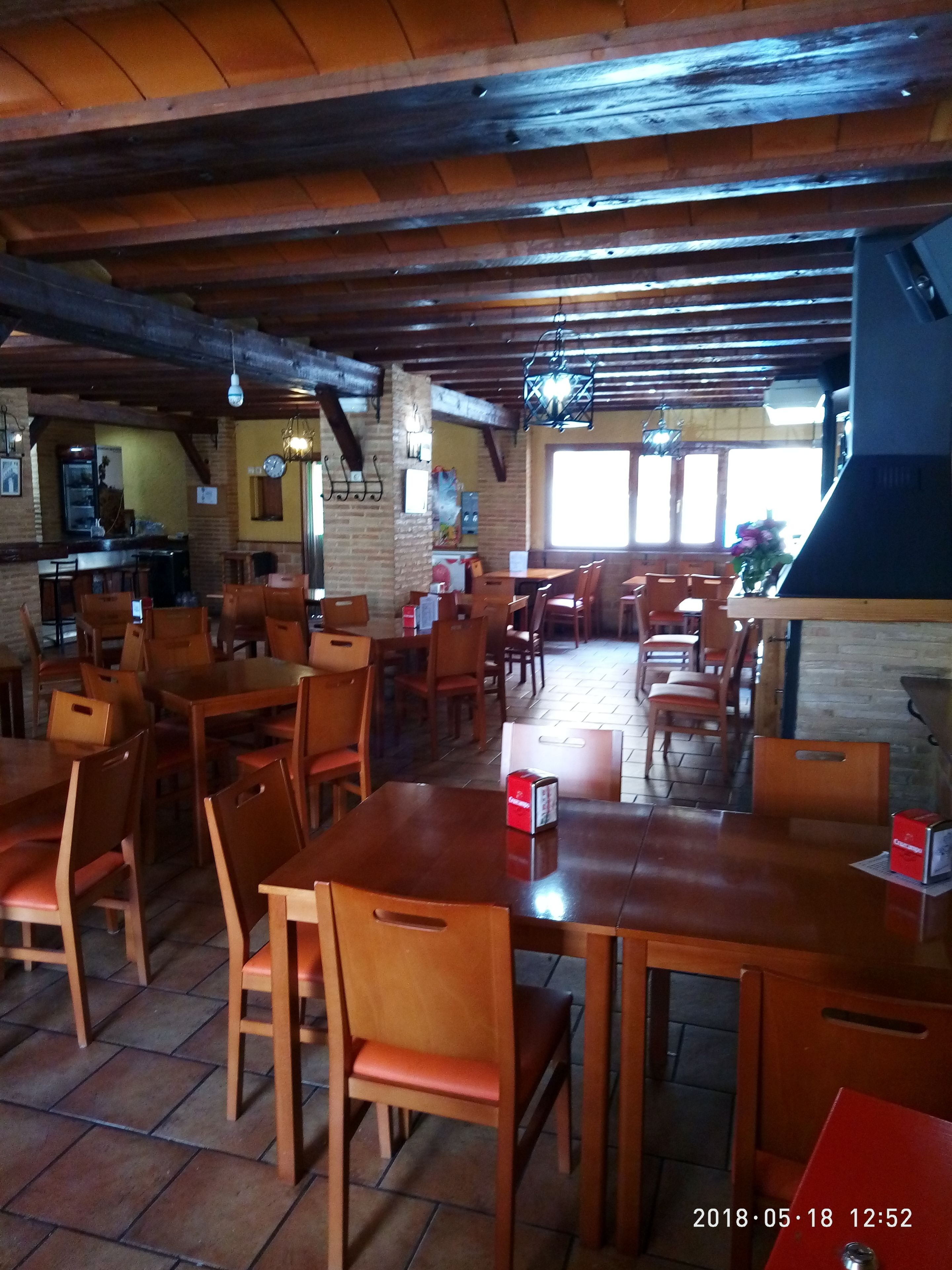 Un restaurante con mesas y sillas de madera, paredes de ladrillo y una gran parrilla negra.