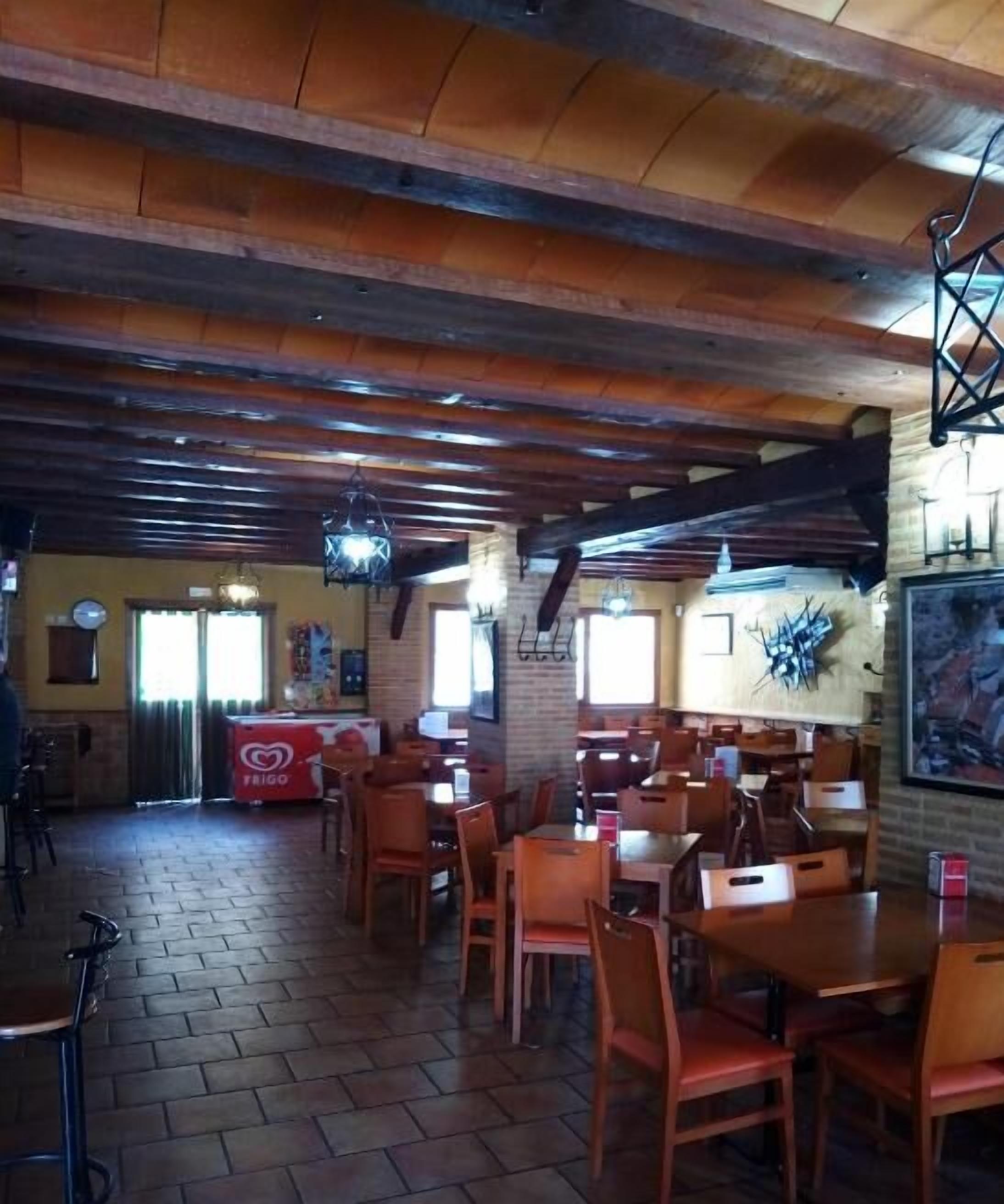 A restaurant with wooden beams on the ceiling, brick walls, and tiled flooring. Tables and chairs are arranged for dining.