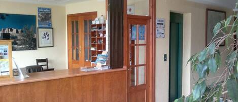 A reception area with a wooden desk, a bookshelf, and a sign indicating directions to the WC and Aseos.