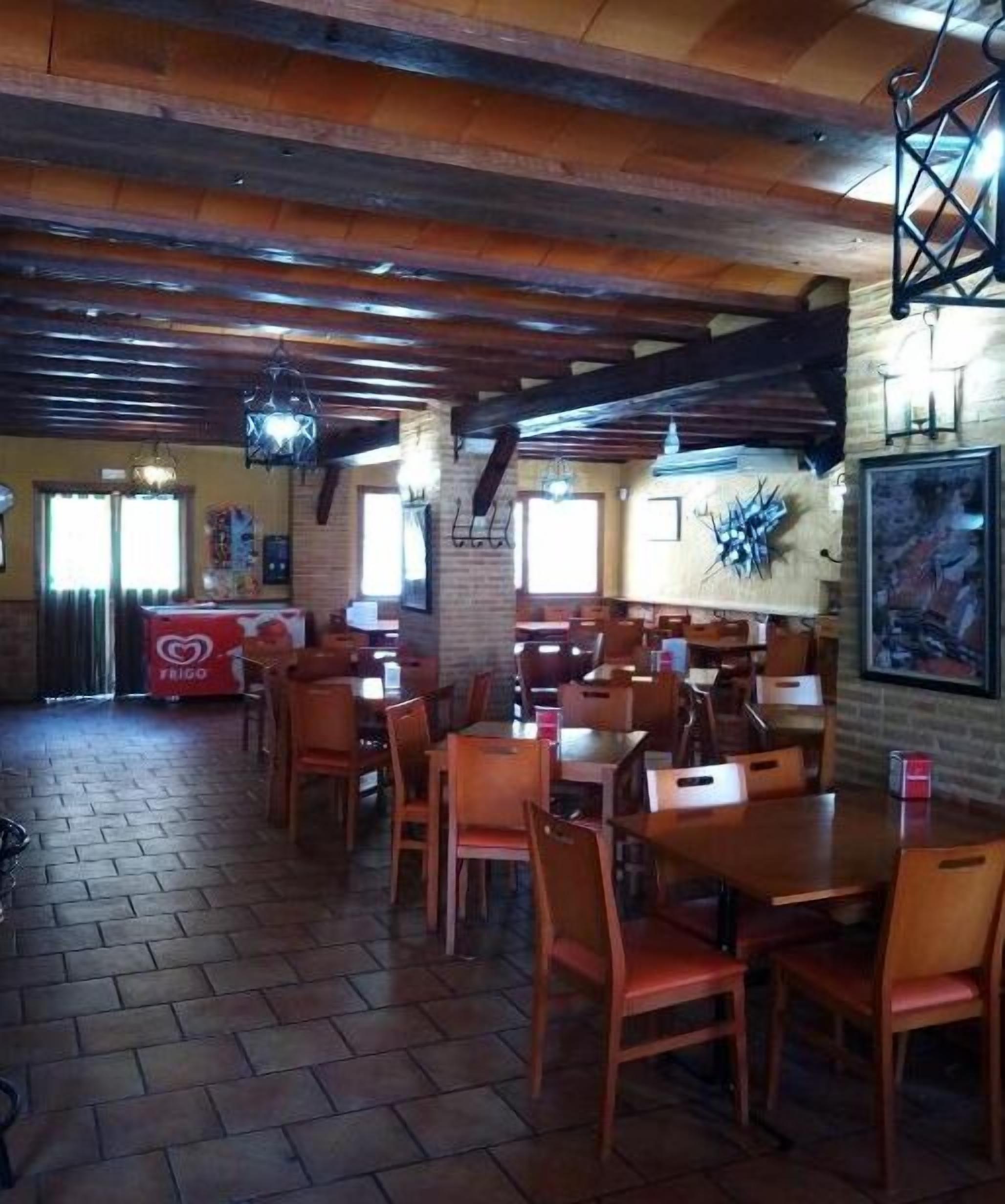 Un restaurante con mesas y sillas de madera, paredes de ladrillo y lámparas colgantes.