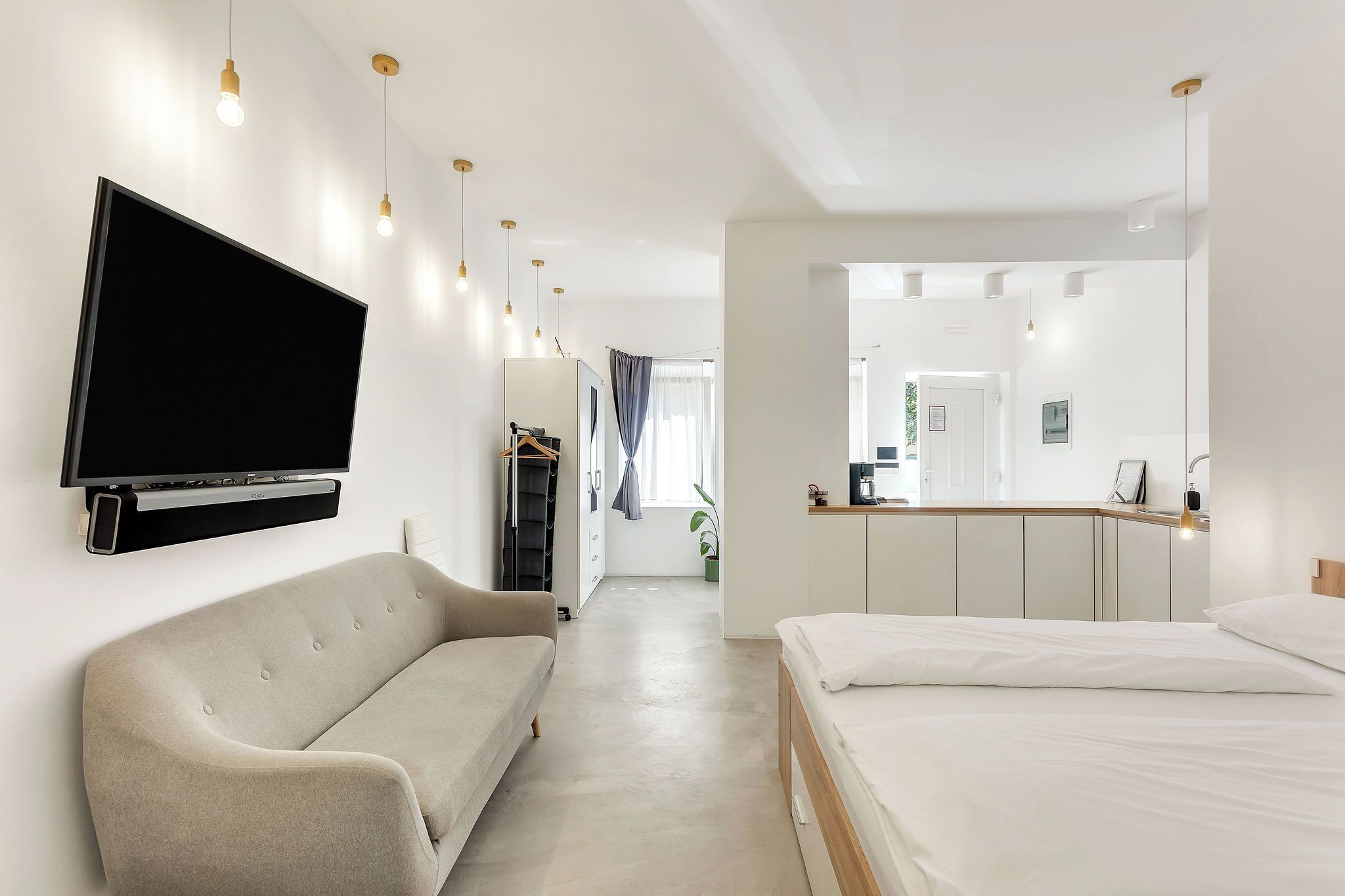 Una habitación de hotel moderna con televisión de pantalla plana montada en la pared, un sofá, una cama y una pequeña zona de kitchenette.