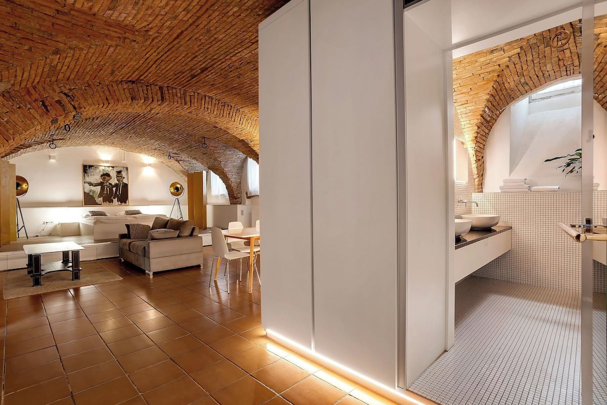 Un intérieur moderne avec un plafond en briques, un canapé blanc, un coin repas et une salle de bain carrelée avec un lavabo.
