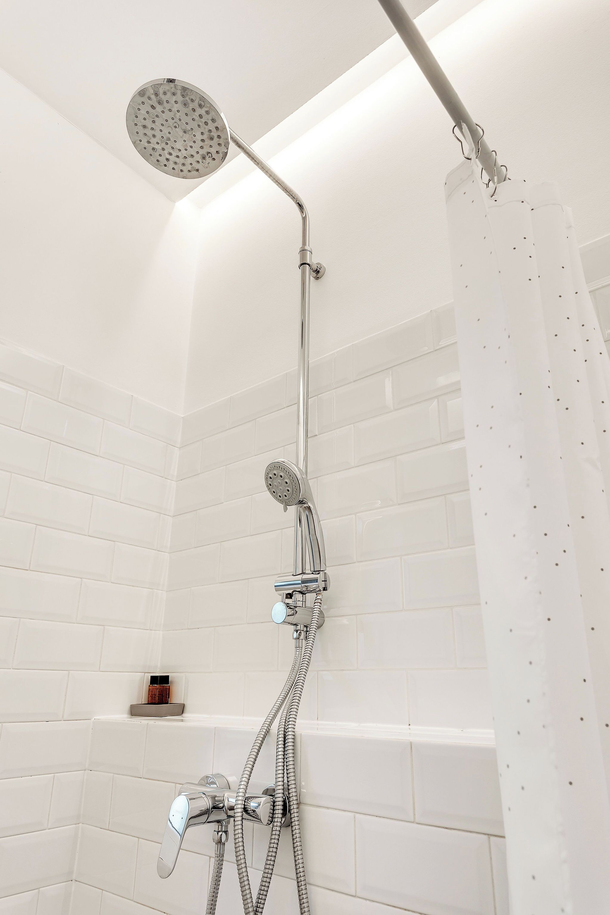A shower with a handheld showerhead, a wall-mounted faucet, and a shower curtain.