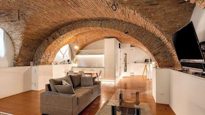 Un loft moderno con arcos de ladrillo visto, una sala de estar con sofá y mesa de centro, y una cocina al fondo.