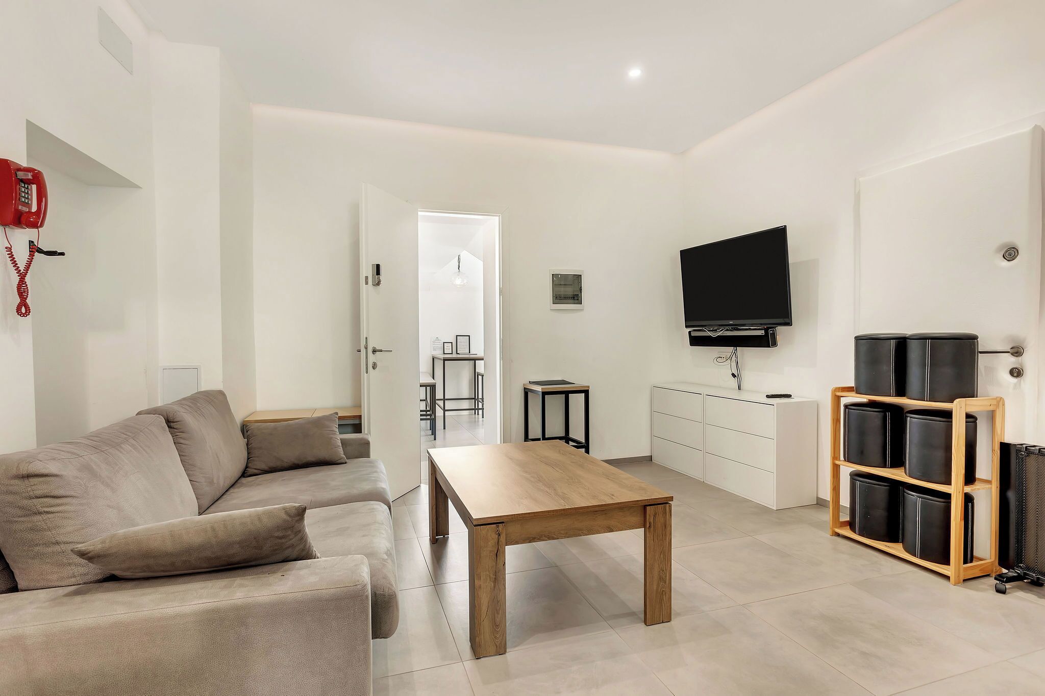 A modern living room with a beige sofa, a wooden coffee table, a TV, and a black speaker system.