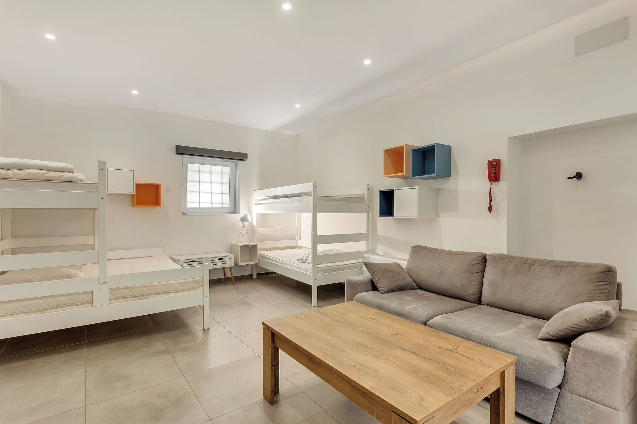 A modern, well-lit room with bunk beds, a sofa, a wooden coffee table, and a desk with a lamp.