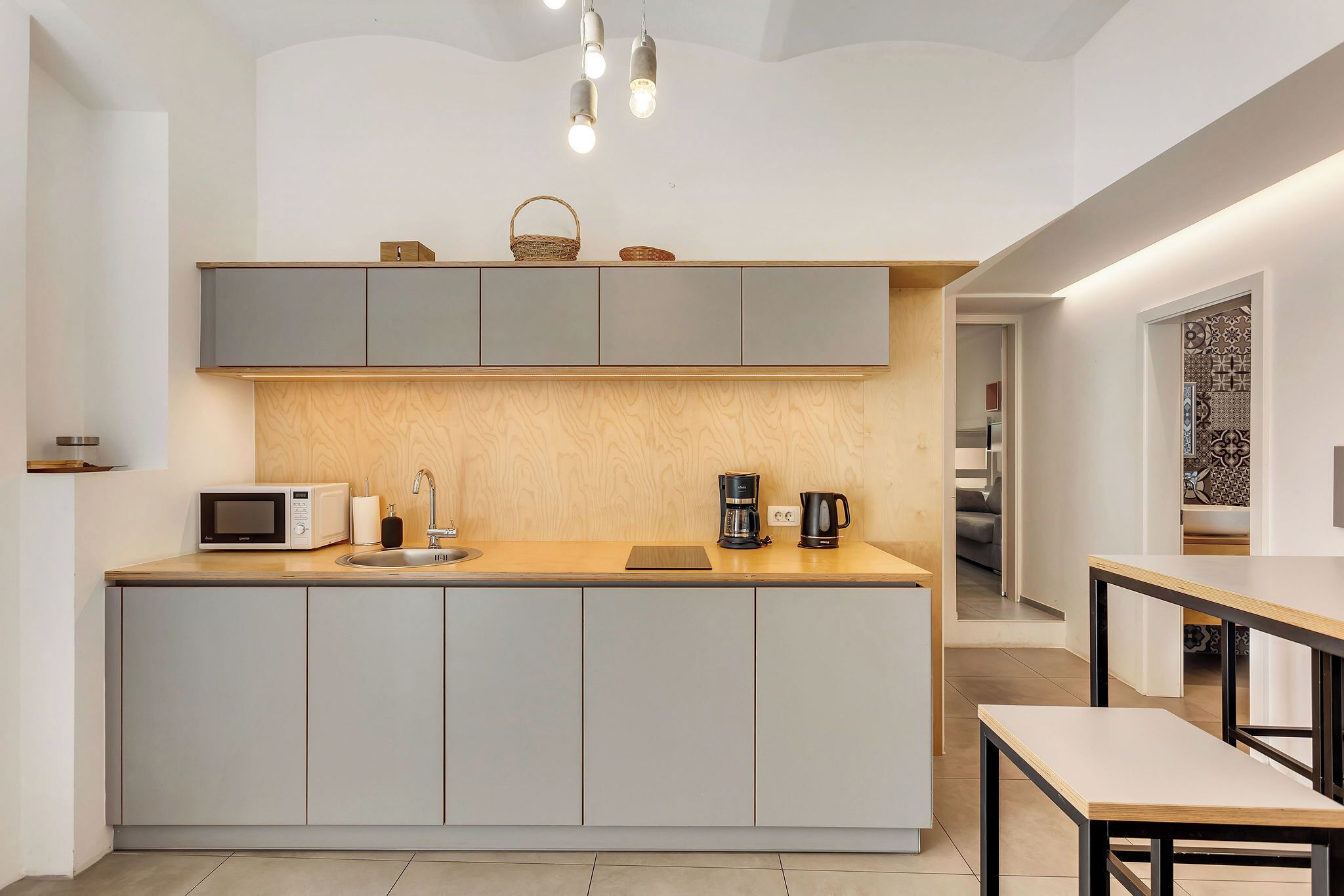A modern kitchen with grey cabinets, a wooden countertop, a microwave, a coffee maker, and hanging pendant lights.