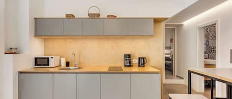 A modern kitchen with grey cabinets, a wooden countertop, a microwave, a coffee maker, and hanging pendant lights.