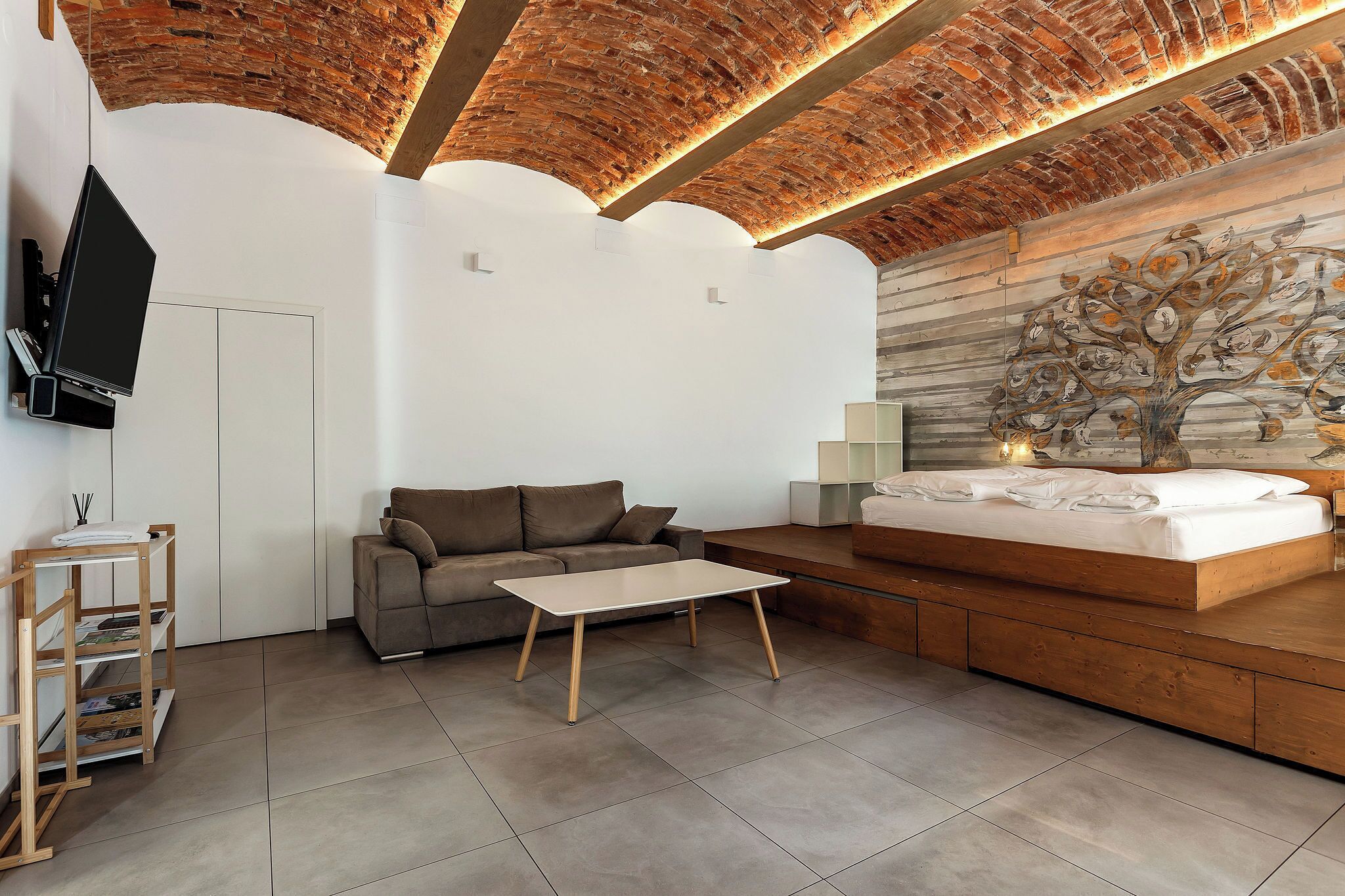 A modern room with a brick ceiling, a bed, a sofa, a coffee table, and a TV.