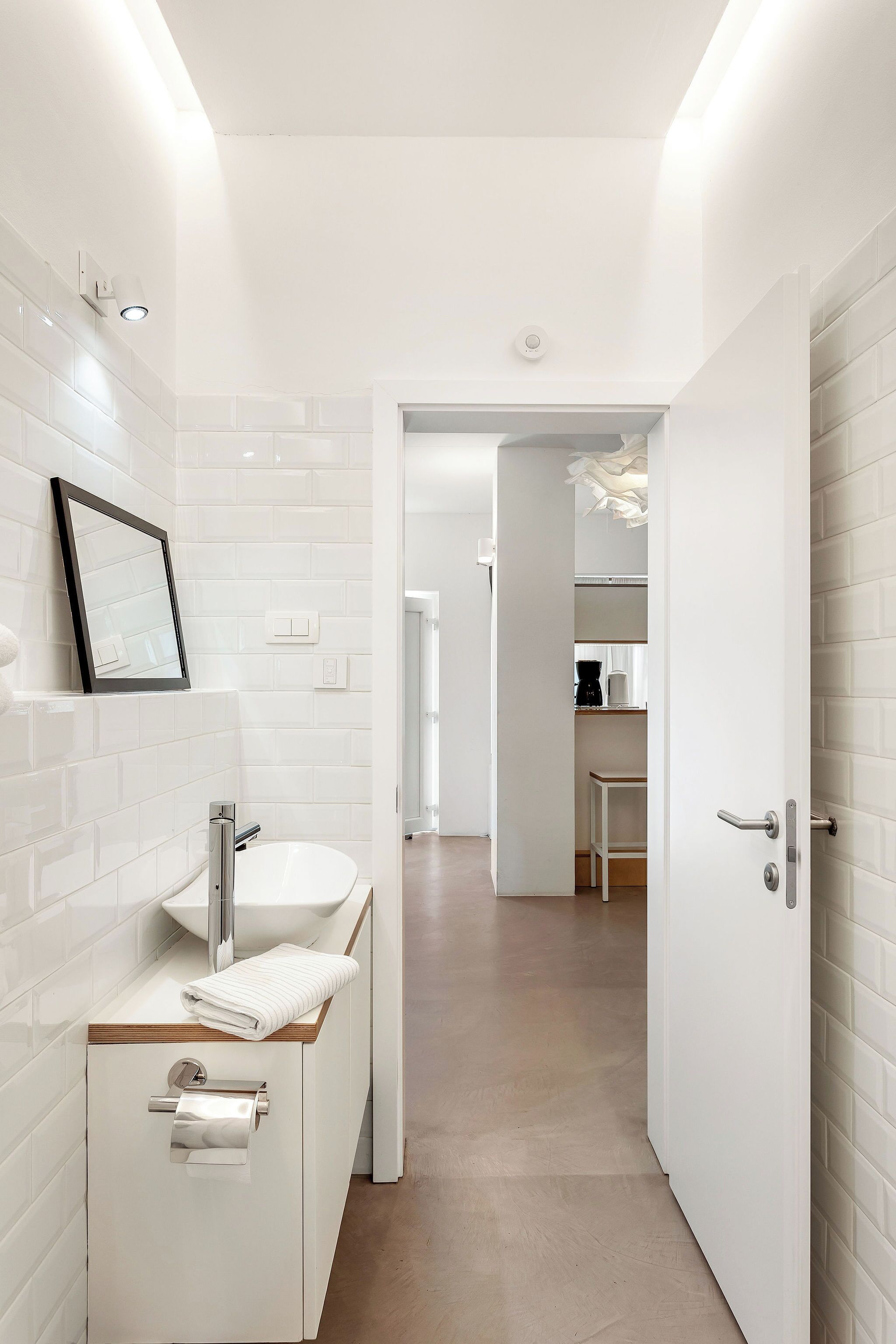 Un baño moderno con azulejos blancos, un lavabo, un espejo y un inodoro.