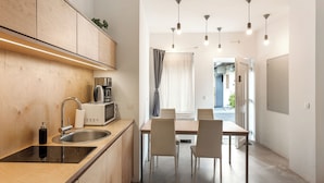 Una cocina moderna con estufa integrada, lavamanos y microondas. Hay un comedor con mesa y sillas, y vistas a la calle a través de amplias ventanas.
