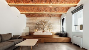 Un dormitorio moderno con techo de ladrillo, una cama con un mural decorativo de un árbol, un sofá, una mesita de noche y una ventana con cortinas.