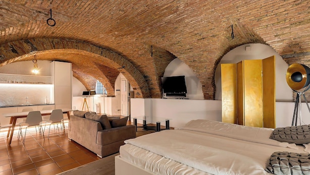 Una habitación amplia con una cama grande, un sofá y un comedor con sillas. La habitación cuenta con techos de ladrillo visto y una zona de cocina moderna.
