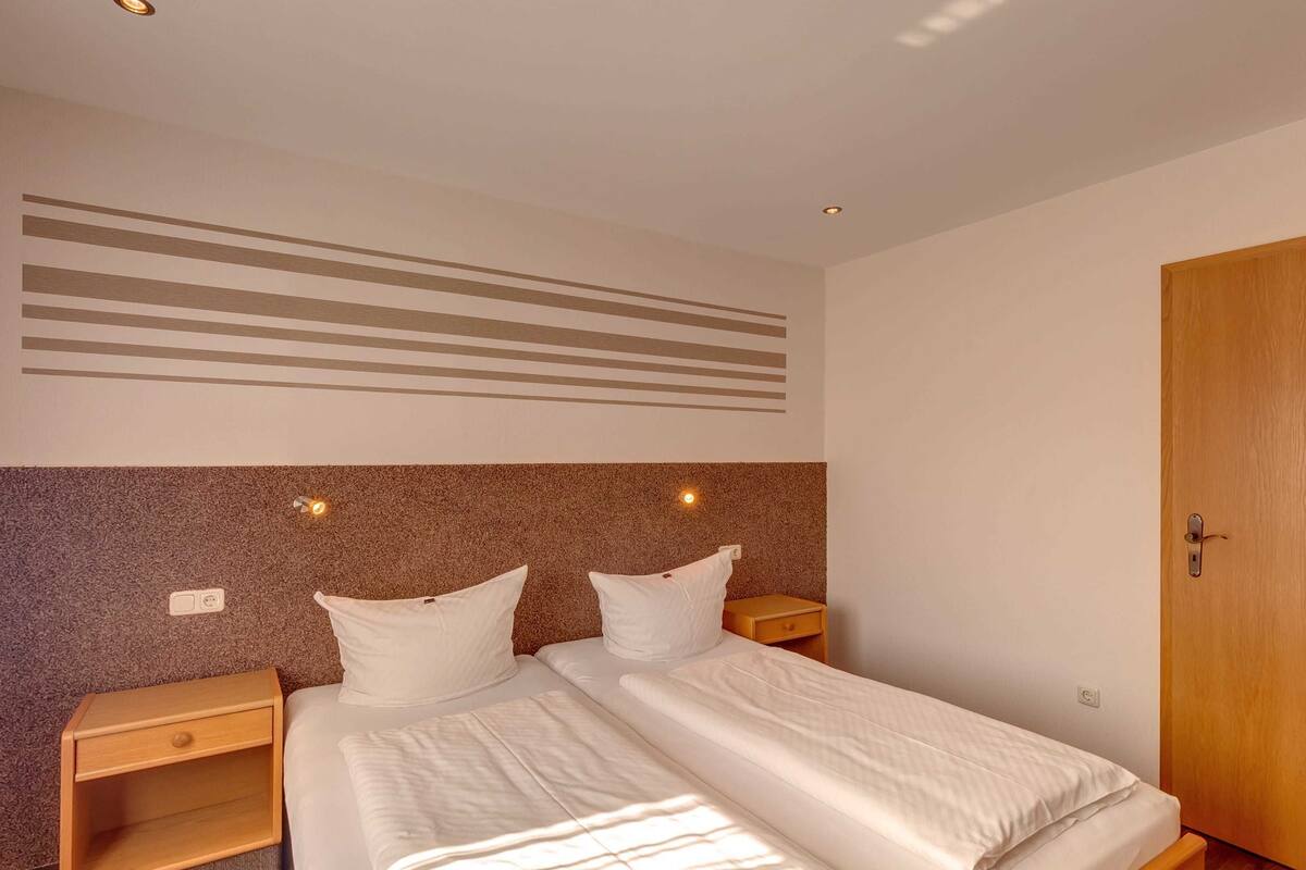 Una cama doble con dos mesitas de noche, una puerta de madera y una pared con rayas horizontales.