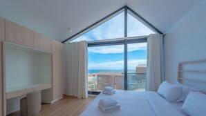A modern hotel room with a large window, a neatly made bed, a wooden wardrobe, and a small trash bin. - VESTA - Soma Bay Residence (Soma Bay)