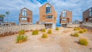 Un edifici modern a la costa, amb façana de pedra, grans finestres i una escala central que condueix a l'entrada.