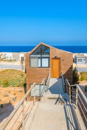 Un edificio moderno con fachada de madera, una escalera que conduce a la entrada y vistas al mar.