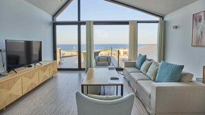 A modern living room with a large window, a flat-screen TV, a sofa, and a dining table. - VESTA - Soma Bay Residence (Soma Bay)