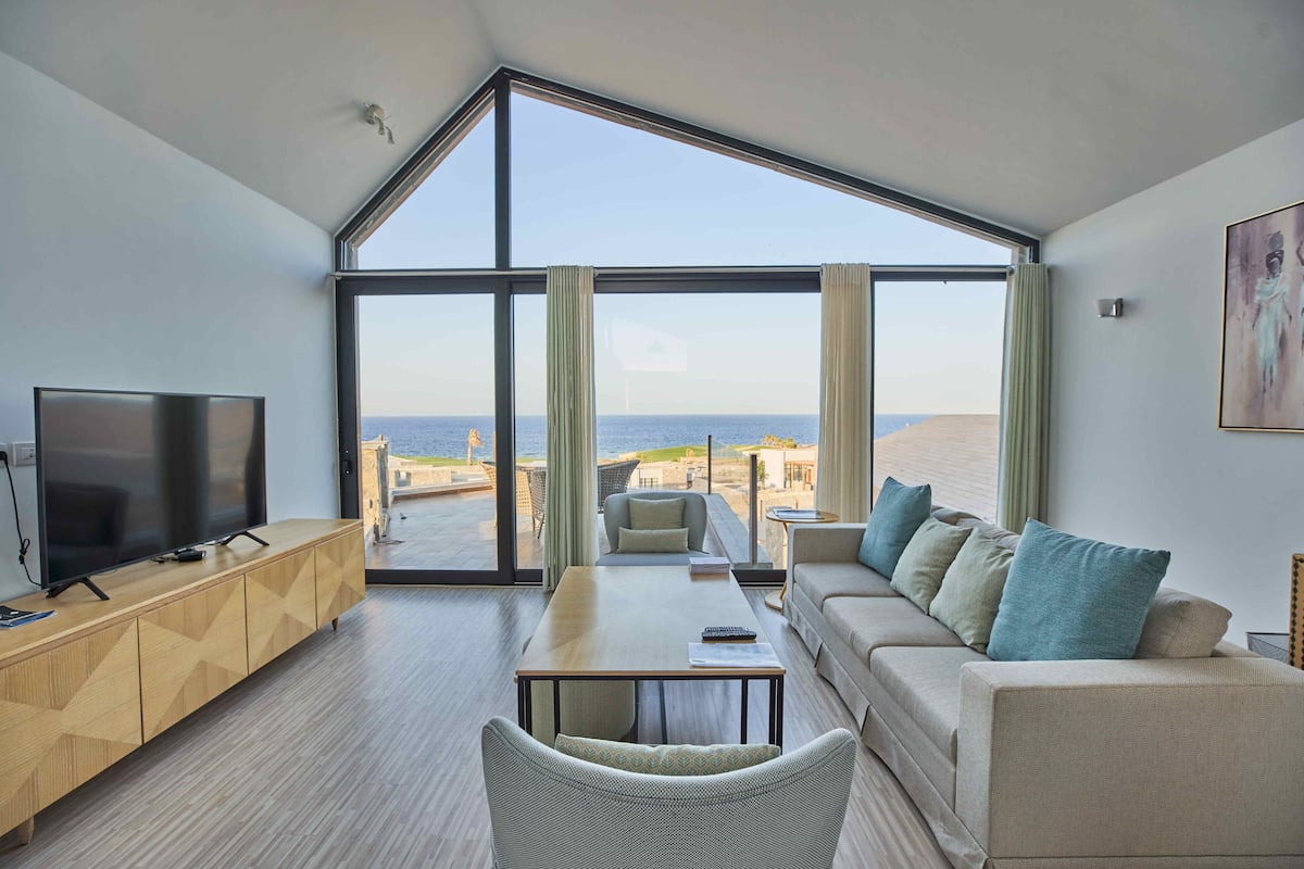 A modern living room with a large window, a flat-screen TV, a sofa, and a dining table.