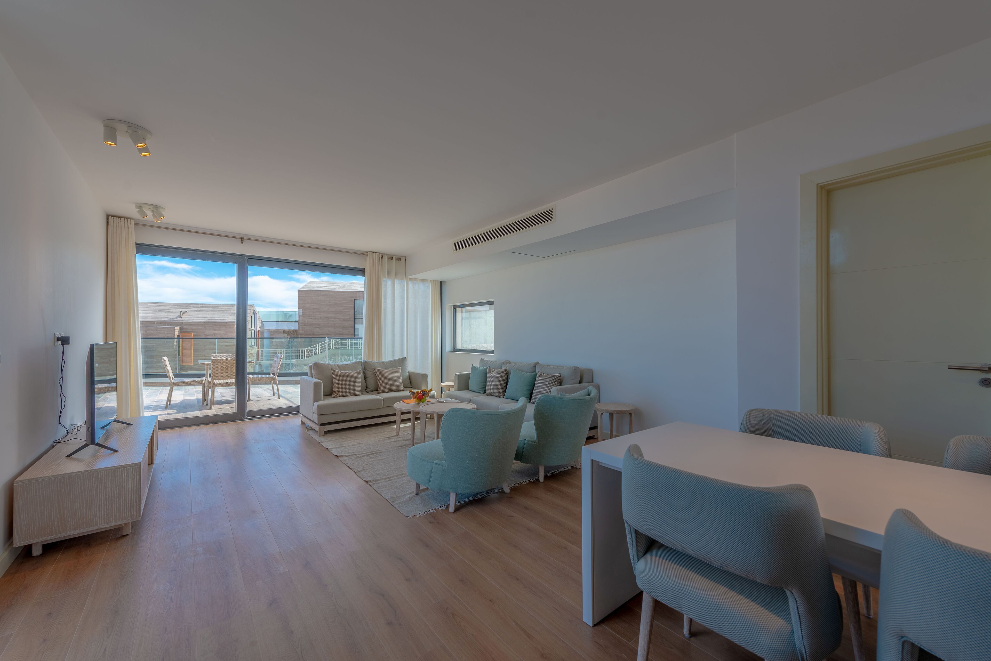 A modern living room with a sofa, chairs, a dining table, and a TV.